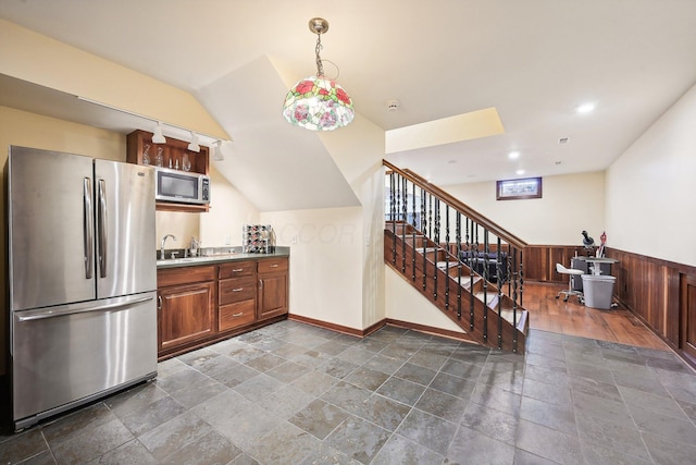 kitchen featuring sink, wood walls, lofted ceiling, decorative light fixtures, and appliances with stainless steel finishes