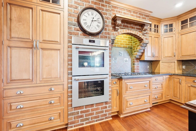 kitchen featuring white double oven, backsplash, light hardwood / wood-style flooring, dark stone countertops, and stainless steel gas cooktop