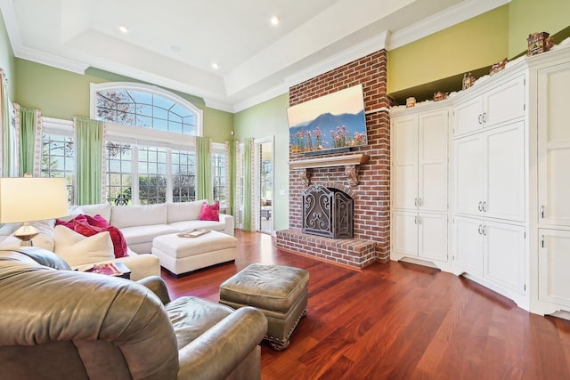 living room featuring a raised ceiling, dark hardwood / wood-style flooring, crown molding, and a brick fireplace