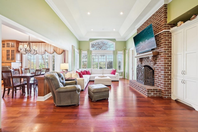 living room featuring a raised ceiling, a chandelier, dark hardwood / wood-style floors, and a brick fireplace