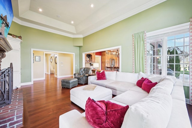 living room featuring a raised ceiling, crown molding, a towering ceiling, dark hardwood / wood-style flooring, and a chandelier