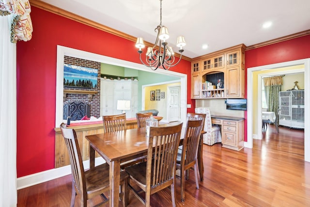 dining room with a fireplace, hardwood / wood-style flooring, ornamental molding, and a notable chandelier