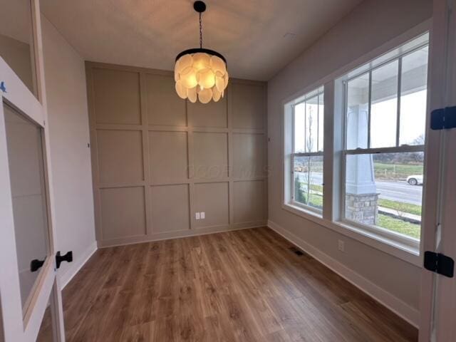 unfurnished dining area featuring a wealth of natural light, hardwood / wood-style floors, and an inviting chandelier