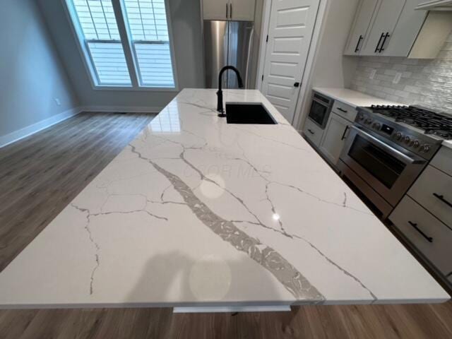 kitchen with light stone countertops, backsplash, stainless steel appliances, sink, and dark hardwood / wood-style floors