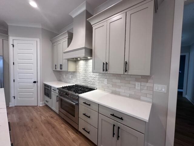 kitchen with custom exhaust hood, backsplash, stainless steel stove, light wood-type flooring, and built in microwave