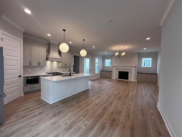 kitchen with tasteful backsplash, decorative light fixtures, gray cabinets, a kitchen island with sink, and custom exhaust hood