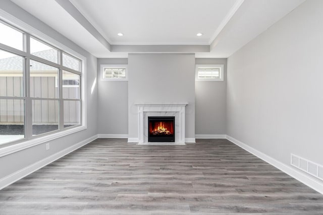 unfurnished living room featuring light wood-type flooring, a tray ceiling, ornamental molding, and a premium fireplace