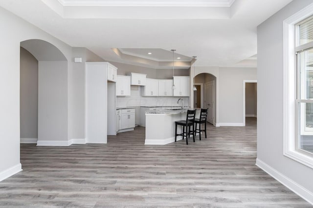 kitchen with white cabinets, a raised ceiling, light hardwood / wood-style flooring, an island with sink, and a breakfast bar area