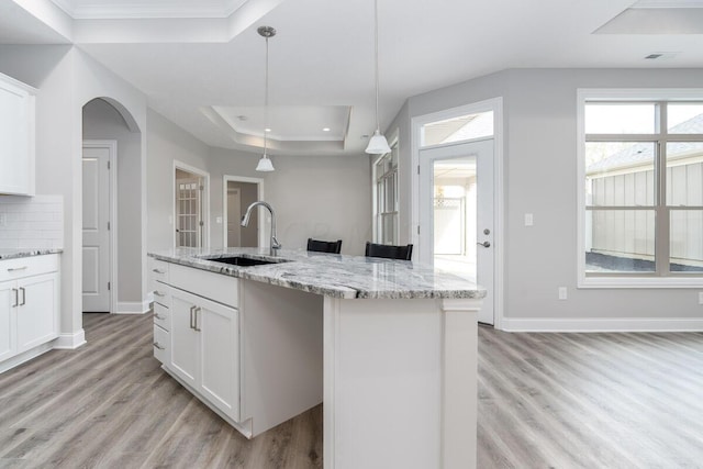 kitchen with light wood-type flooring, a raised ceiling, sink, decorative light fixtures, and white cabinetry