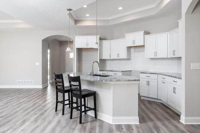 kitchen with a raised ceiling, sink, a center island with sink, light hardwood / wood-style floors, and white cabinetry