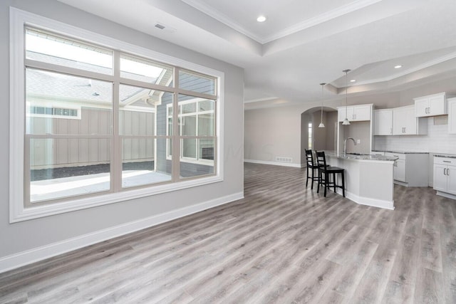 kitchen featuring a center island with sink, a raised ceiling, white cabinetry, and light wood-type flooring