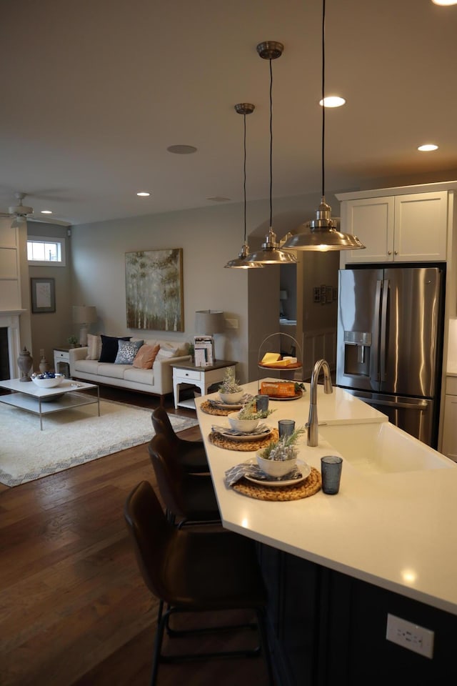 kitchen featuring ceiling fan, dark hardwood / wood-style flooring, stainless steel fridge, pendant lighting, and white cabinets