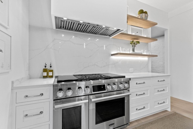 kitchen featuring light wood-type flooring, backsplash, stainless steel range, extractor fan, and white cabinetry