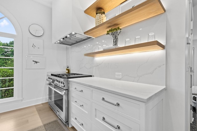 kitchen with custom exhaust hood, white cabinets, high end stainless steel range oven, decorative backsplash, and light hardwood / wood-style floors