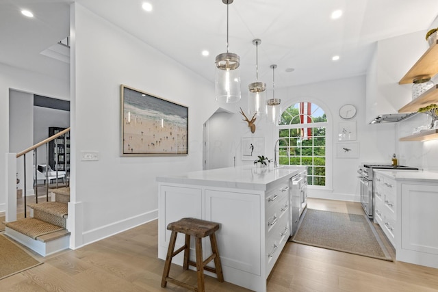 kitchen featuring appliances with stainless steel finishes, light hardwood / wood-style floors, white cabinetry, and a kitchen island with sink