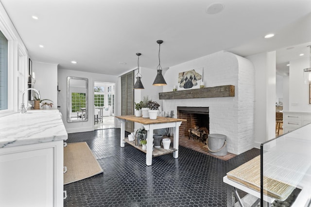 interior space with light stone counters, sink, a fireplace, white cabinetry, and hanging light fixtures