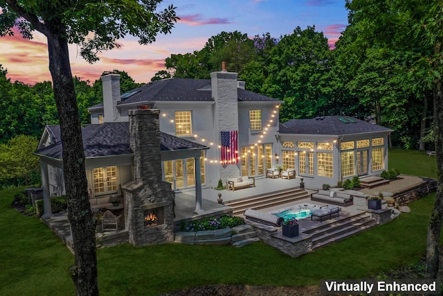 back house at dusk with an outdoor stone fireplace, a yard, and a patio