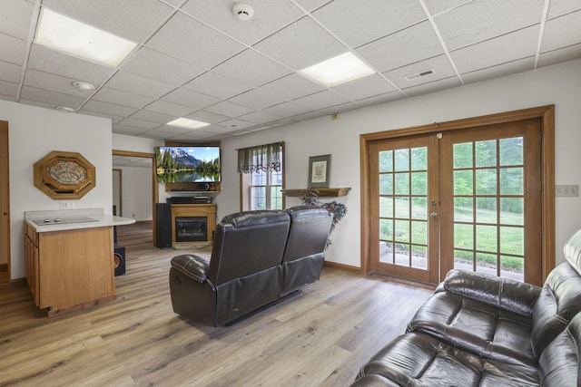 living room with a drop ceiling, a healthy amount of sunlight, and light wood-type flooring