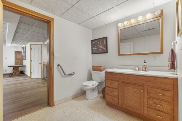 bathroom featuring toilet, vanity, a drop ceiling, and hardwood / wood-style flooring