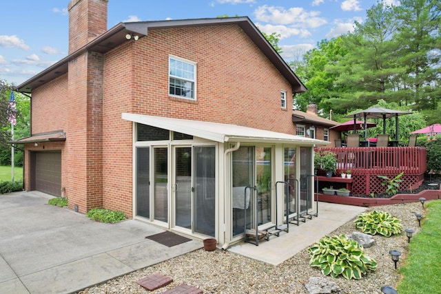 rear view of property with a sunroom, a garage, and a wooden deck