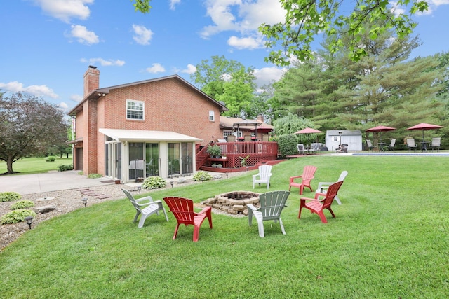 rear view of house featuring a lawn, a sunroom, a fire pit, a storage unit, and a wooden deck