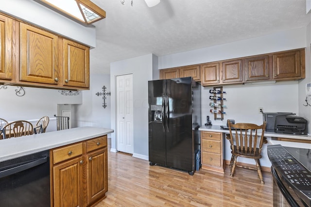 kitchen featuring a textured ceiling, light hardwood / wood-style flooring, built in desk, and black appliances