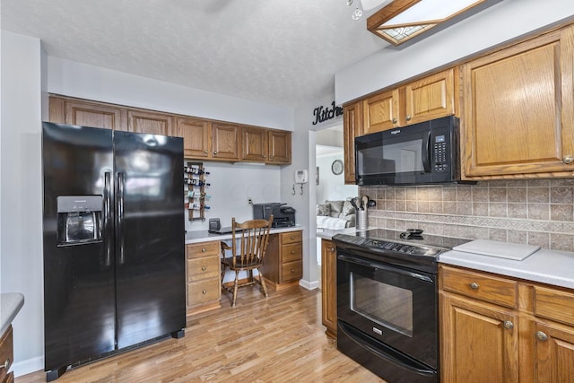 kitchen featuring black appliances, built in desk, light wood-type flooring, a textured ceiling, and tasteful backsplash