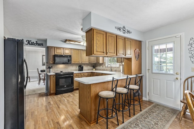 kitchen with kitchen peninsula, a healthy amount of sunlight, black appliances, and light hardwood / wood-style floors