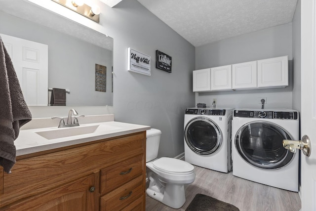 clothes washing area featuring washer and clothes dryer, light wood-type flooring, a textured ceiling, and sink