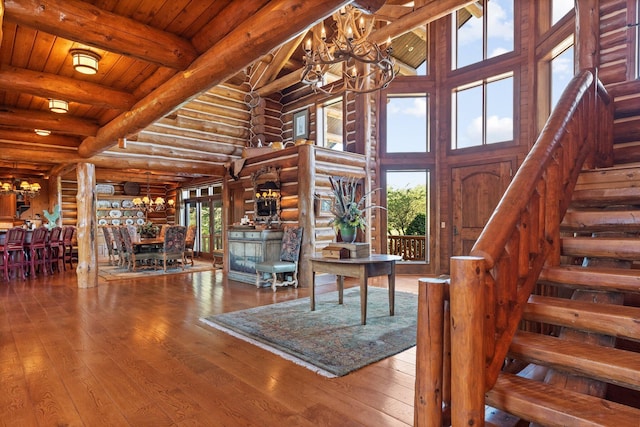 living room featuring wood-type flooring, high vaulted ceiling, an inviting chandelier, and rustic walls