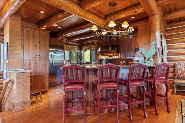 kitchen featuring wooden ceiling, an inviting chandelier, wall chimney range hood, and built in refrigerator