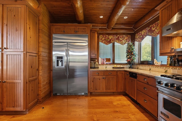 kitchen featuring wall chimney exhaust hood, light wood-type flooring, beamed ceiling, premium appliances, and light stone counters