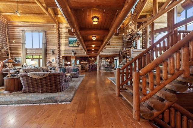 unfurnished living room with wood ceiling, ceiling fan with notable chandelier, log walls, beam ceiling, and hardwood / wood-style flooring