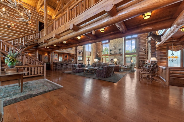 unfurnished living room with log walls, a high ceiling, beamed ceiling, hardwood / wood-style floors, and wood ceiling