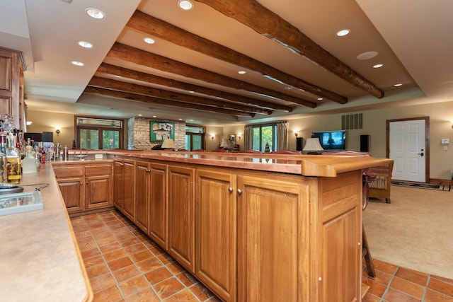 kitchen with kitchen peninsula, light carpet, stovetop, and beamed ceiling