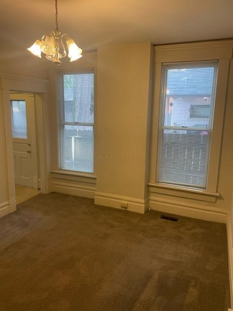 unfurnished dining area with dark carpet, a healthy amount of sunlight, and an inviting chandelier