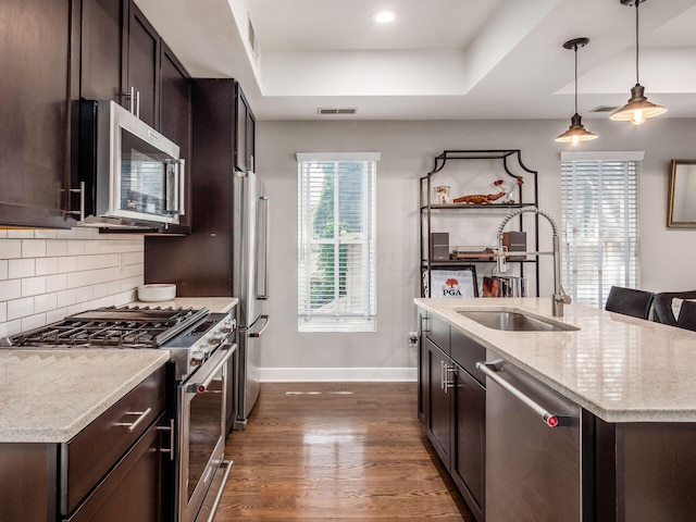 kitchen featuring light stone countertops, appliances with stainless steel finishes, a tray ceiling, decorative light fixtures, and dark hardwood / wood-style flooring