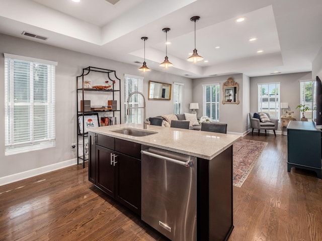 kitchen with stainless steel dishwasher, dark hardwood / wood-style floors, an island with sink, pendant lighting, and a tray ceiling