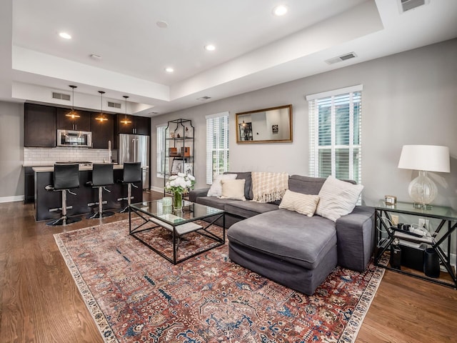 living room featuring dark wood-type flooring, a tray ceiling, and a healthy amount of sunlight