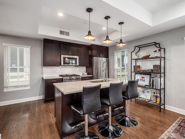 kitchen with a raised ceiling, high quality appliances, pendant lighting, and dark hardwood / wood-style floors