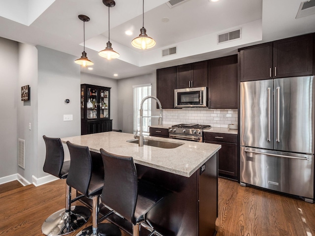 kitchen featuring a kitchen island with sink, sink, light stone counters, premium appliances, and dark hardwood / wood-style flooring