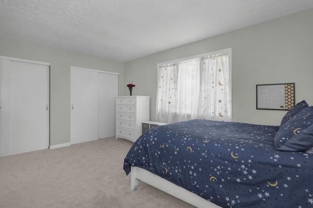 carpeted bedroom featuring a textured ceiling and multiple closets