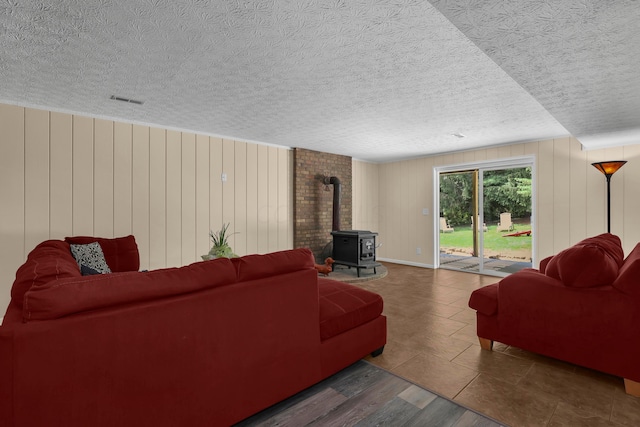 living room featuring wood walls, a wood stove, a textured ceiling, and dark wood-type flooring