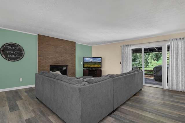 living room featuring dark hardwood / wood-style floors, crown molding, a textured ceiling, and a brick fireplace