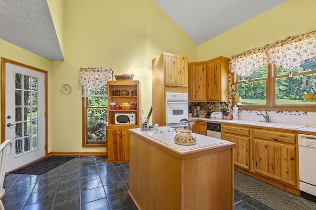 kitchen with a wealth of natural light, a center island, dark tile patterned flooring, and white appliances