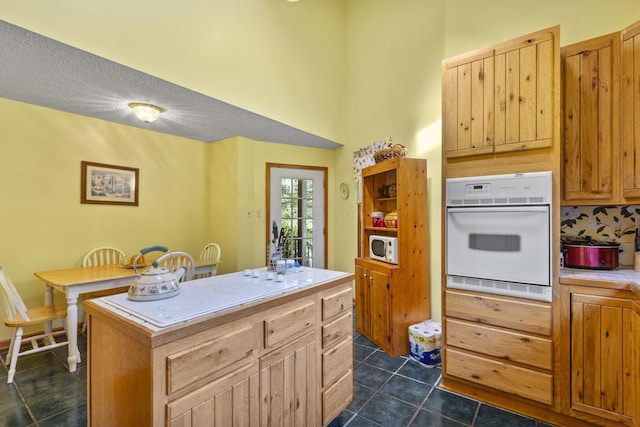 kitchen with light brown cabinets, white appliances, dark tile patterned floors, a textured ceiling, and a kitchen island