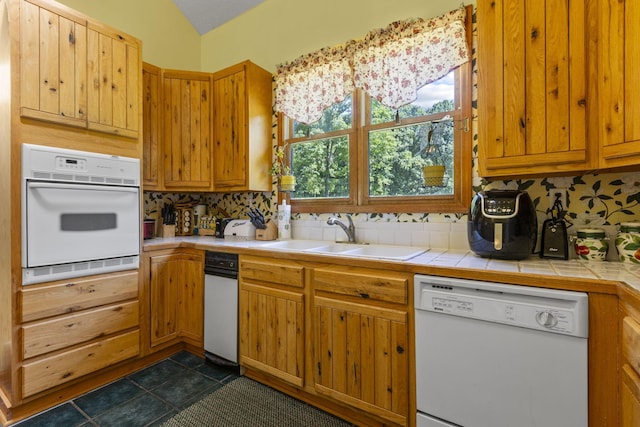 kitchen featuring tile counters, sink, tasteful backsplash, vaulted ceiling, and white appliances