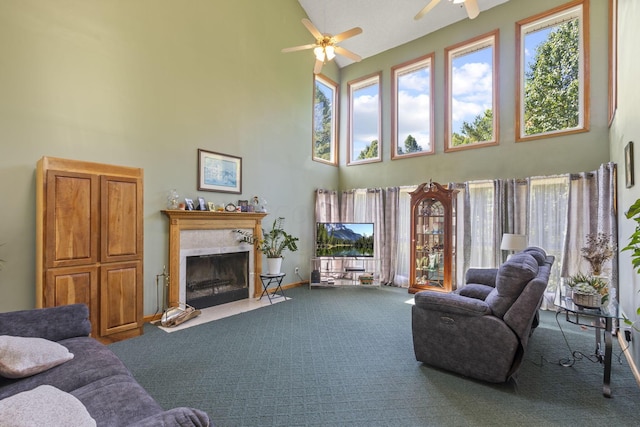 living room featuring carpet flooring, ceiling fan, a fireplace, and a towering ceiling