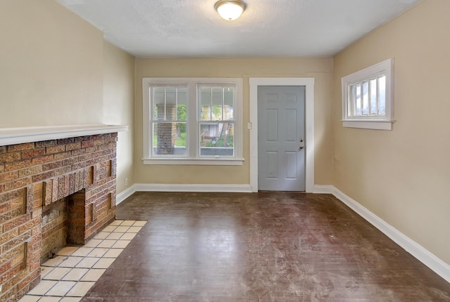 entryway with a textured ceiling, light hardwood / wood-style floors, a brick fireplace, and a wealth of natural light