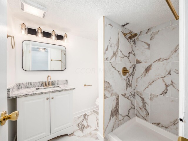 bathroom with a tile shower, vanity, and a textured ceiling